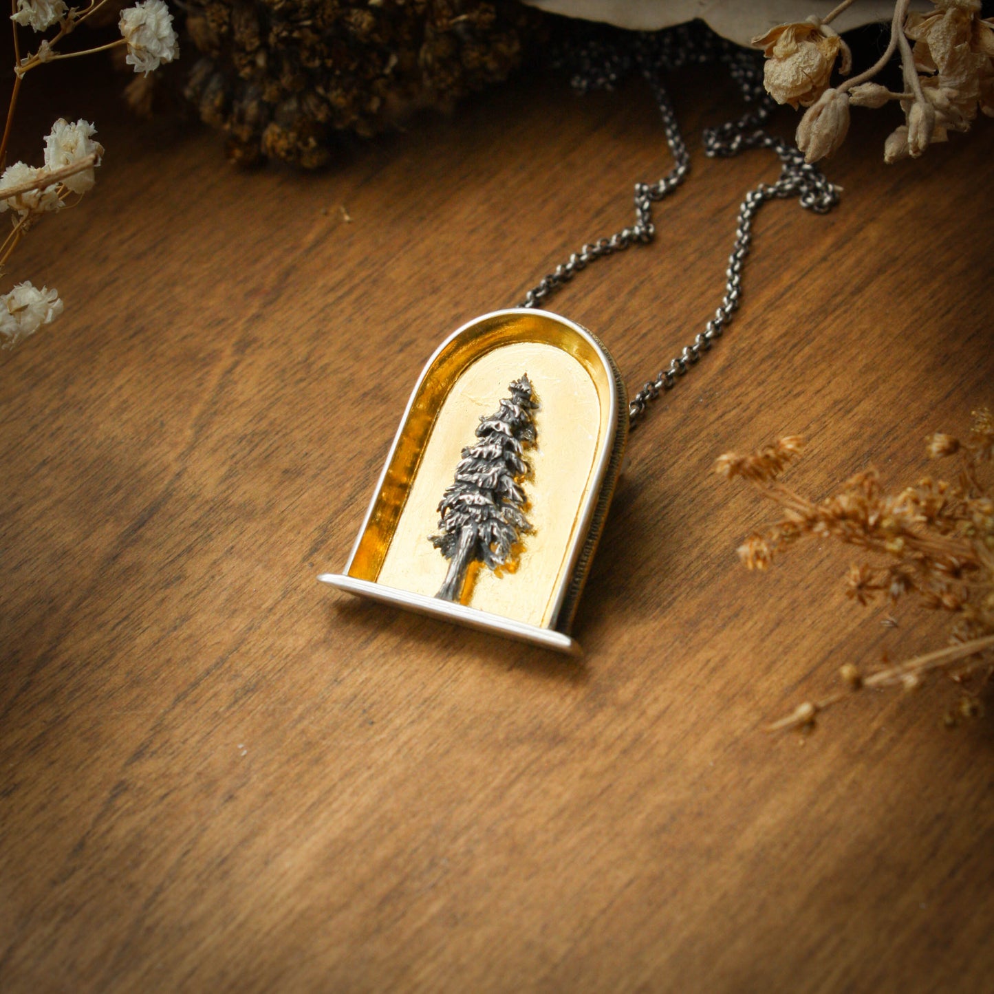 A sterling silver and 24k gold necklace in an arch shape featuring a layered sterlign silver redwood tree with a wood background